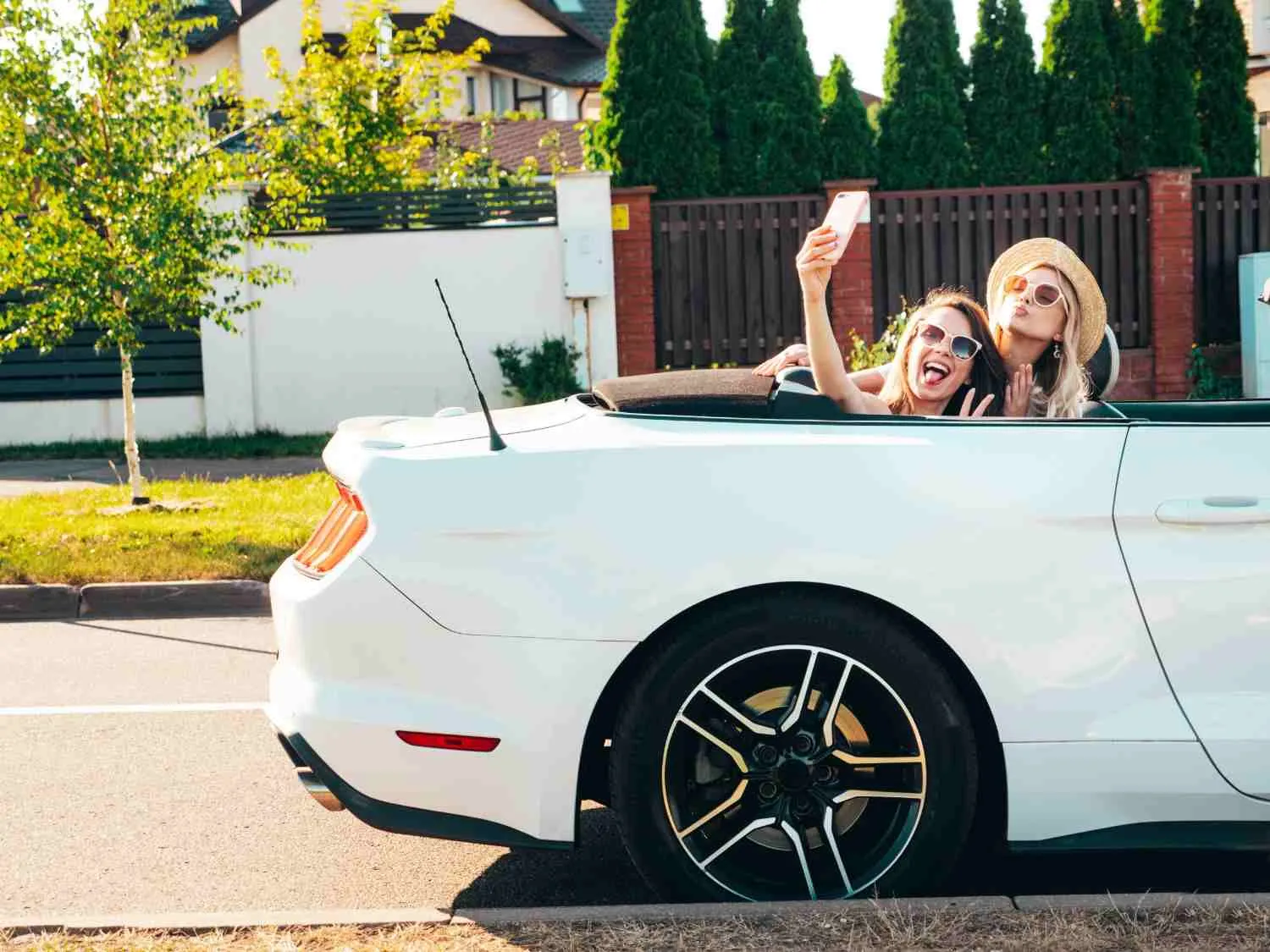 Two friends in a white convertible parked on a quiet street